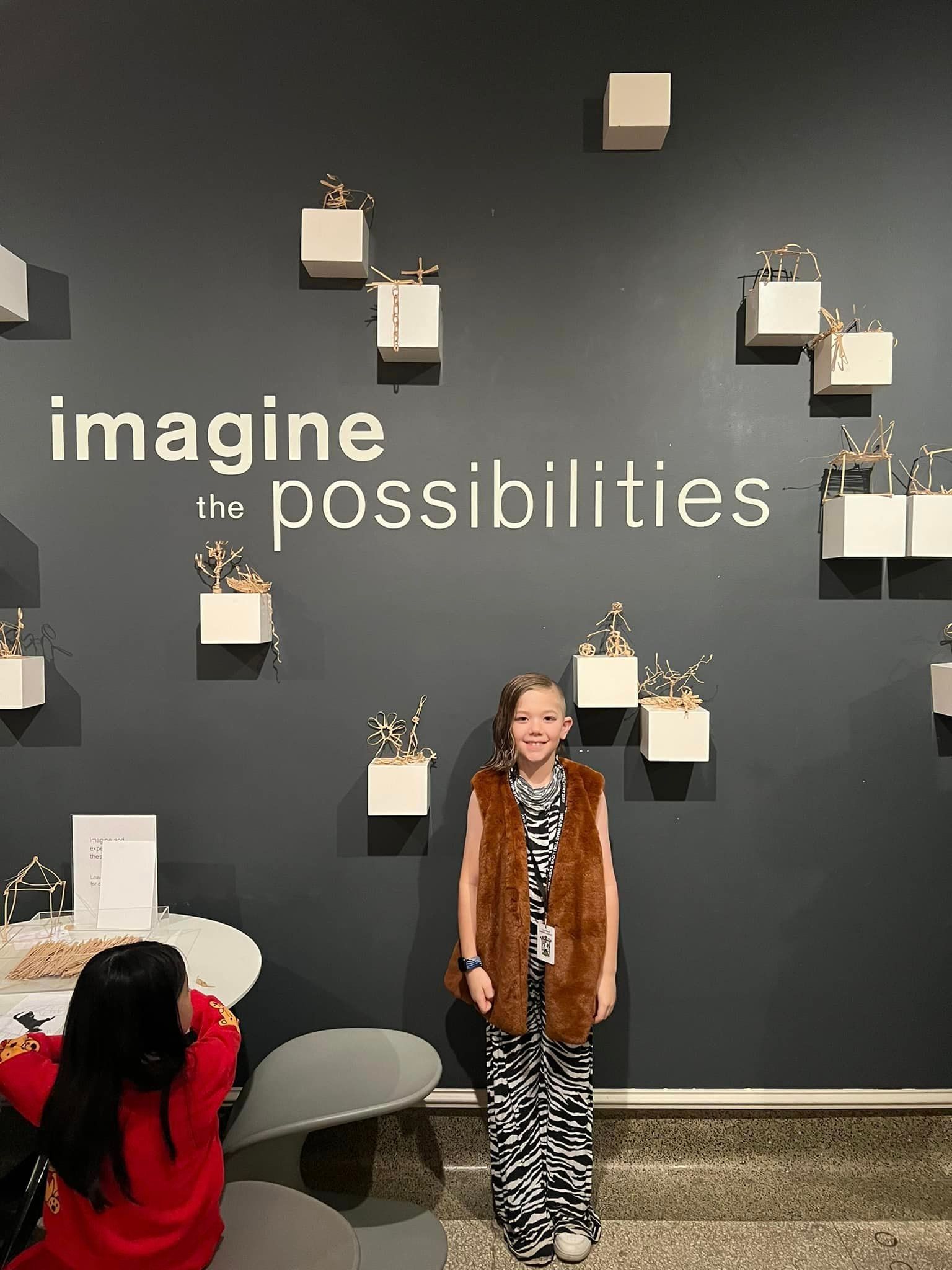 A little boy is standing in front of a wall that says `` imagine possibilities ''.