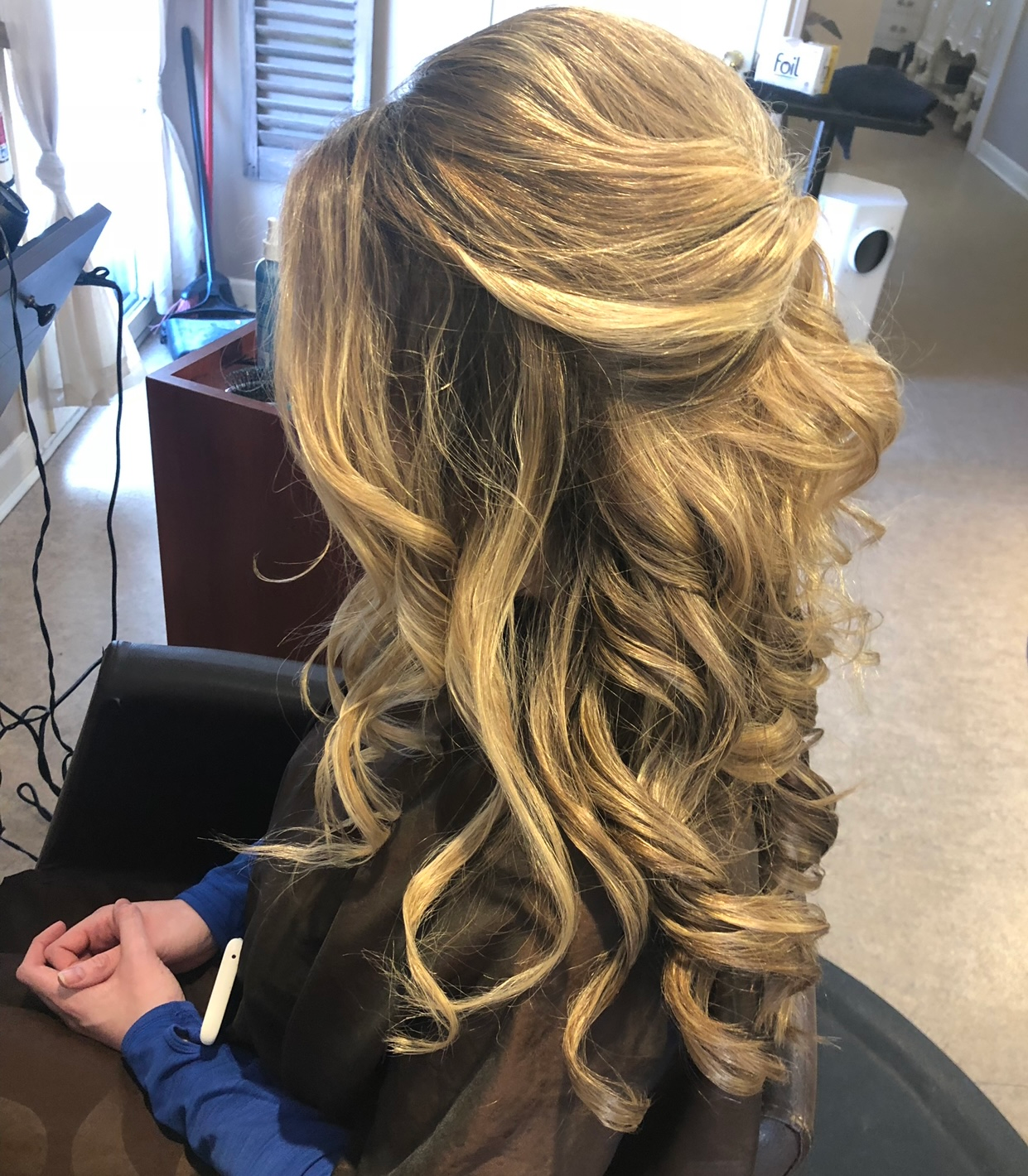 Blonde hair styled in loose curls and a half-updo, sitting in a salon chair.