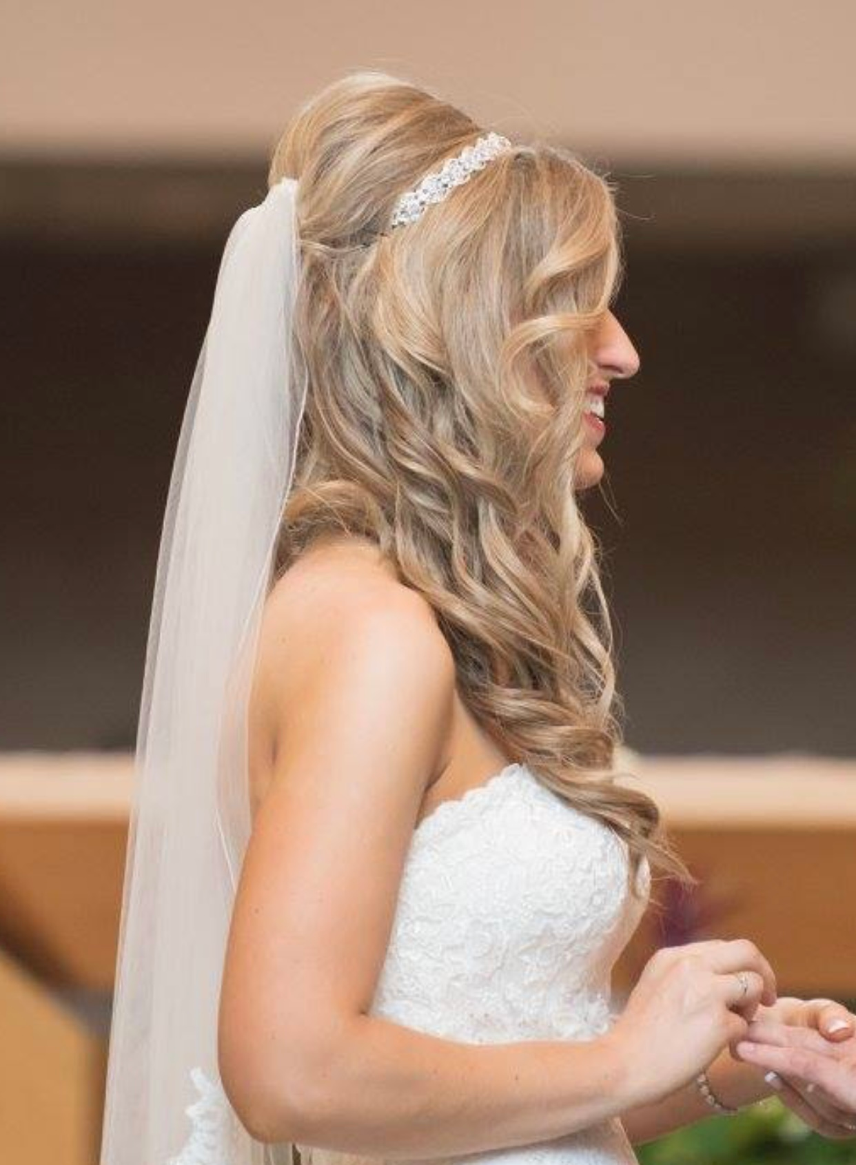 Bride with blonde hair in a wedding dress, wearing a veil and tiara, smiling.