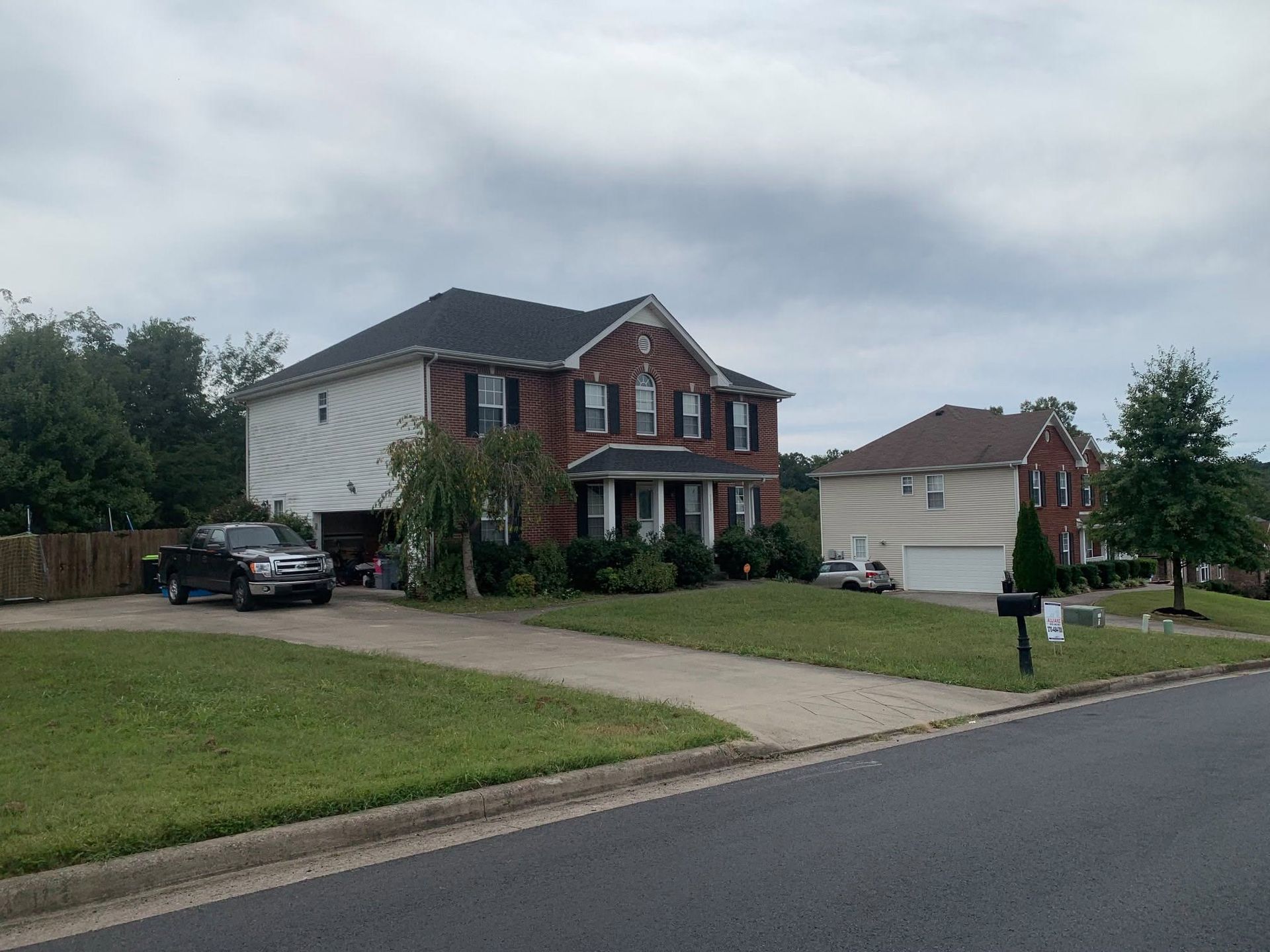 Suburban two-story house with white siding, brick front, driveway, lawn, and parked car under cloudy sky