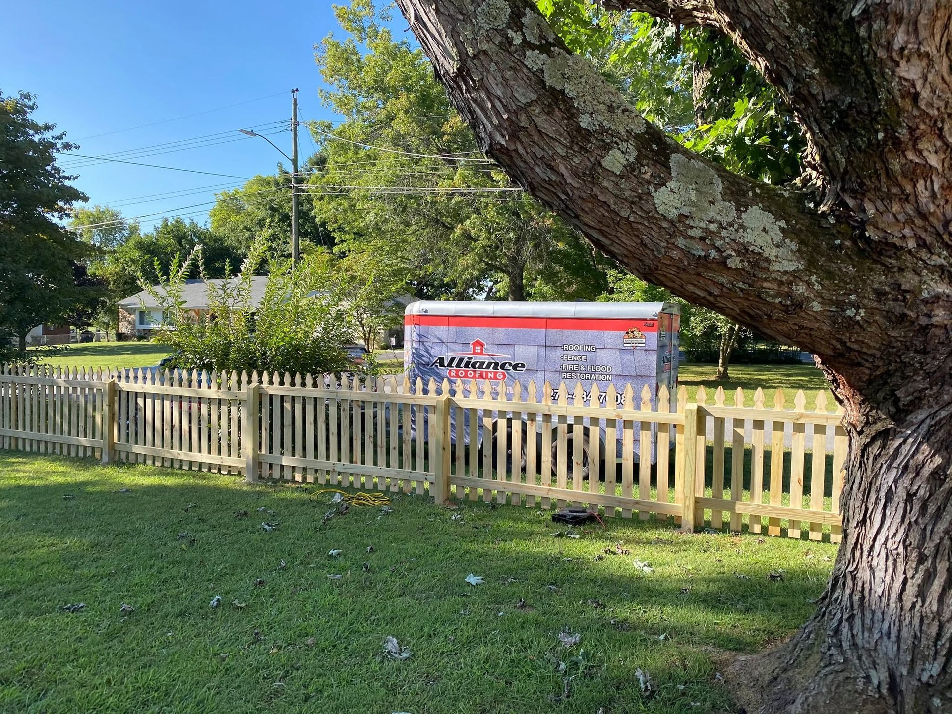 Fenced park with a tree in the foreground and a red-and-white signboard in the background