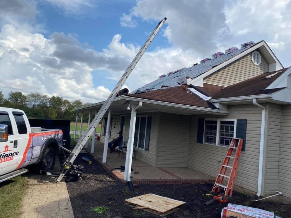 Damaged house roof with a crane, ladder, and work truck in the driveway after storm damage