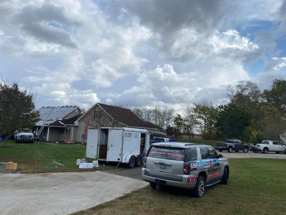 Suburban street with a utility truck and box trailer parked near a house under cloudy skies