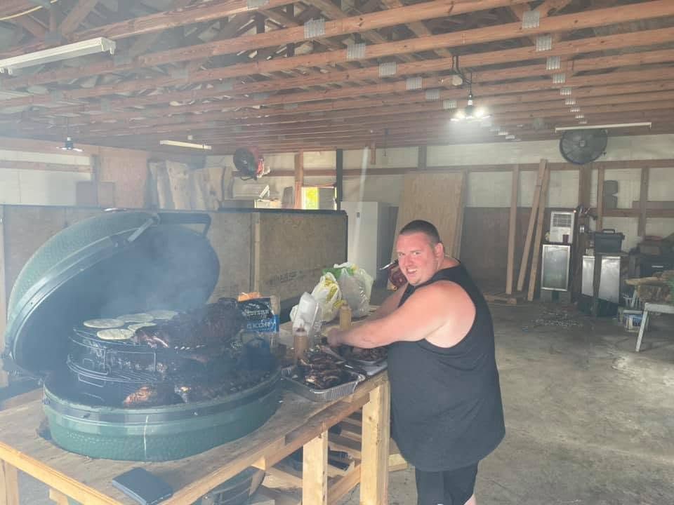 Person grilling meat on a large round barbecue in a rustic indoor workspace