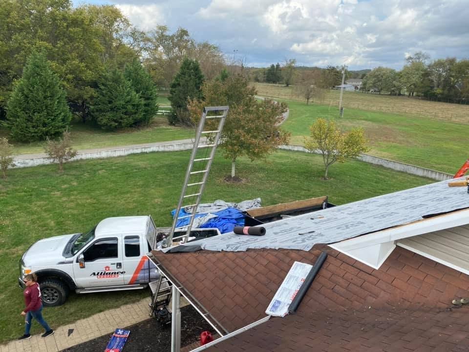 Roof repair scene with white pickup, ladder, and workers on a house roof under cloudy sky