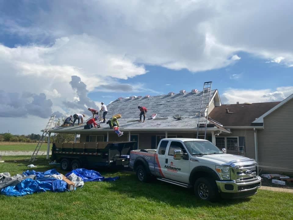 Workers repairing storm-damaged roof beside a pickup truck under a cloudy sky
