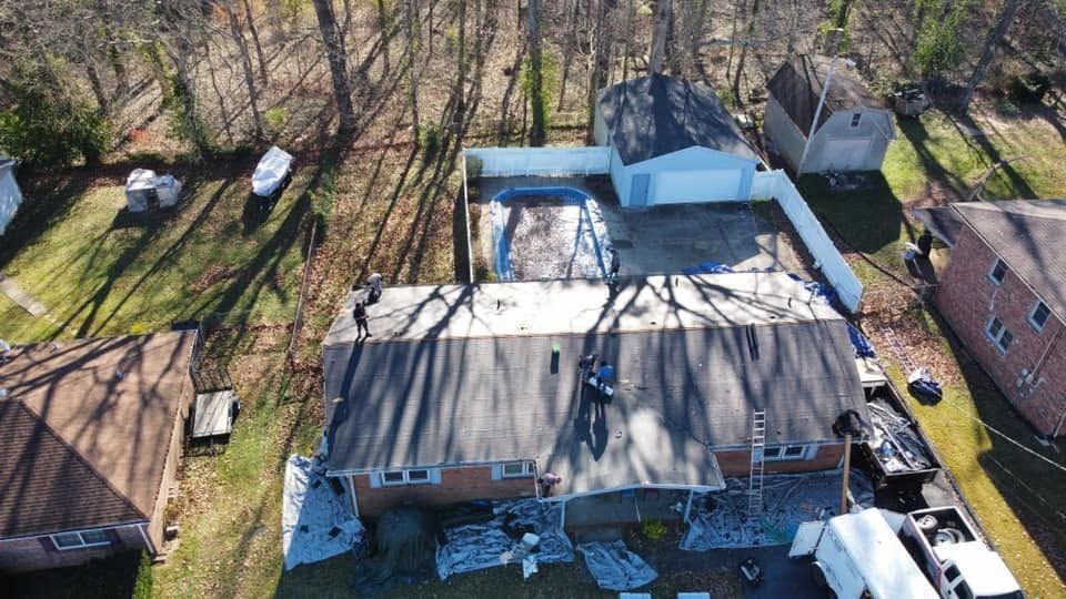 Aerial view of a house with a large roof, surrounded by leafless trees and parked cars.