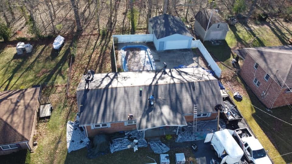 Aerial view of a house with a damaged roof, surrounded by trees and neighboring homes.