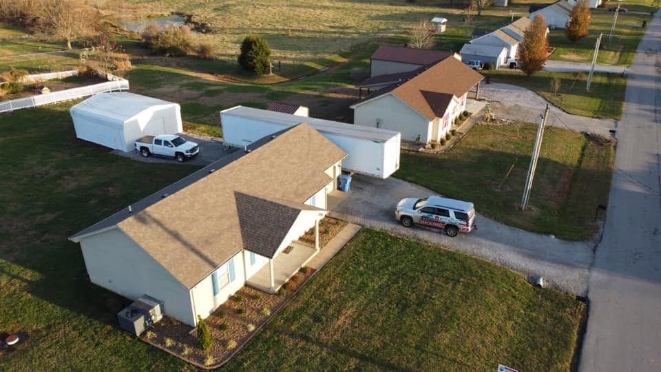 Aerial view of rural homes with parked vehicles beside a paved road and grassy yards