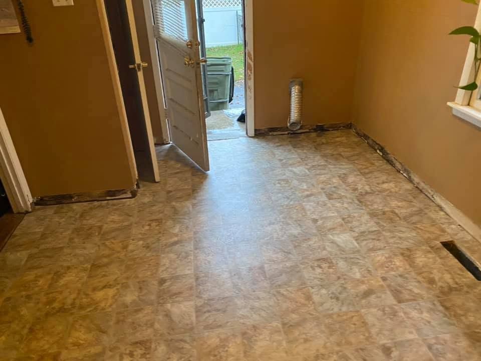 Empty room with worn linoleum floor, tan walls, and an open door to a bright outside area