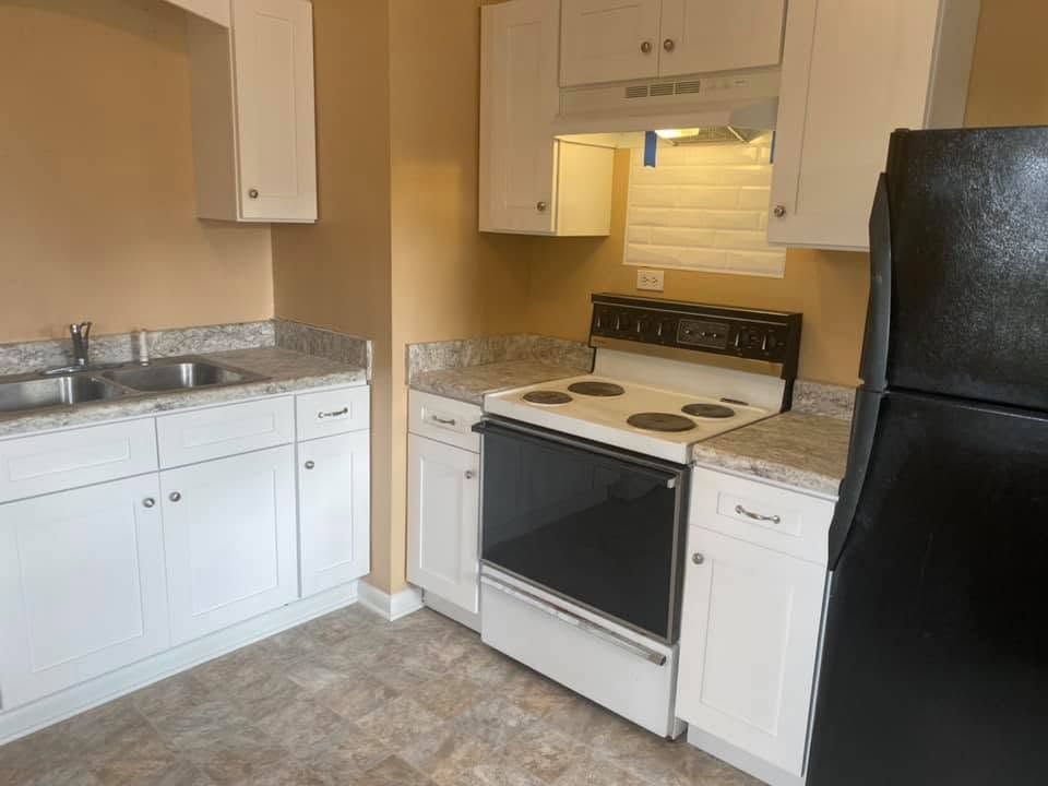 Small white kitchen with black appliances, granite counters, and a tiled floor.