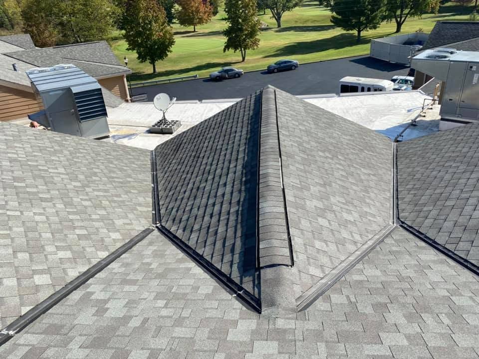 Aerial view of gray shingled rooftops with vents and satellite dishes near a tree-lined street.