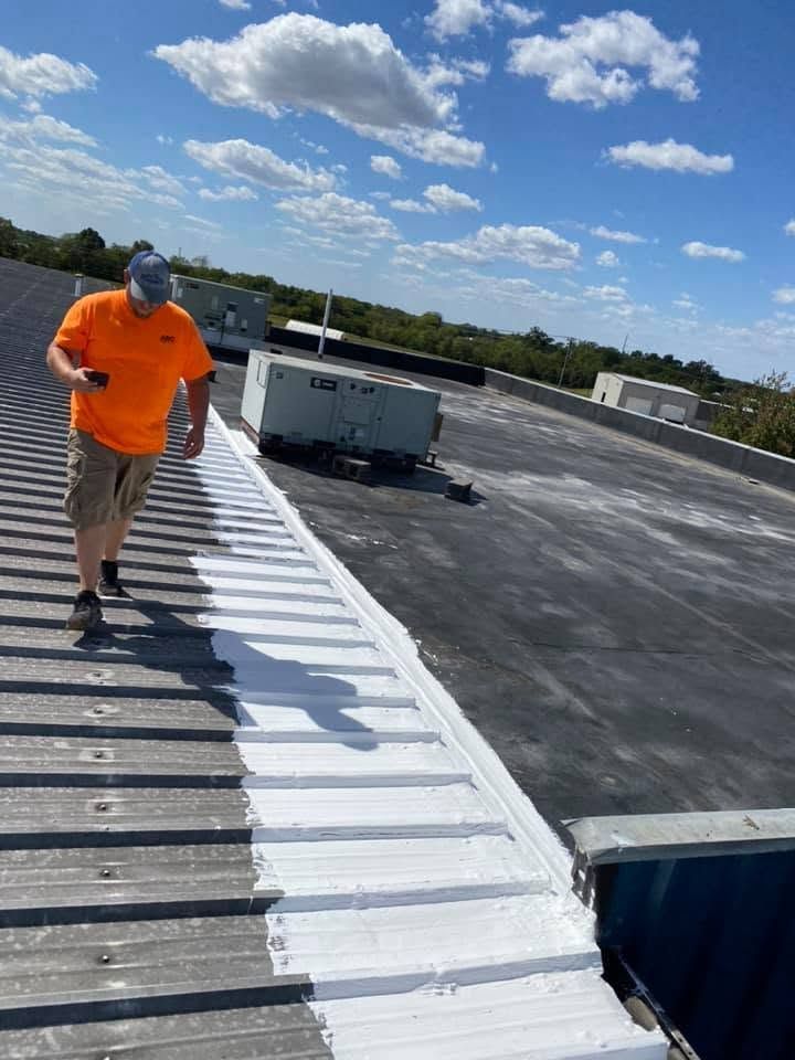 Worker in orange shirt walking on a rooftop under a bright blue sky with clouds.