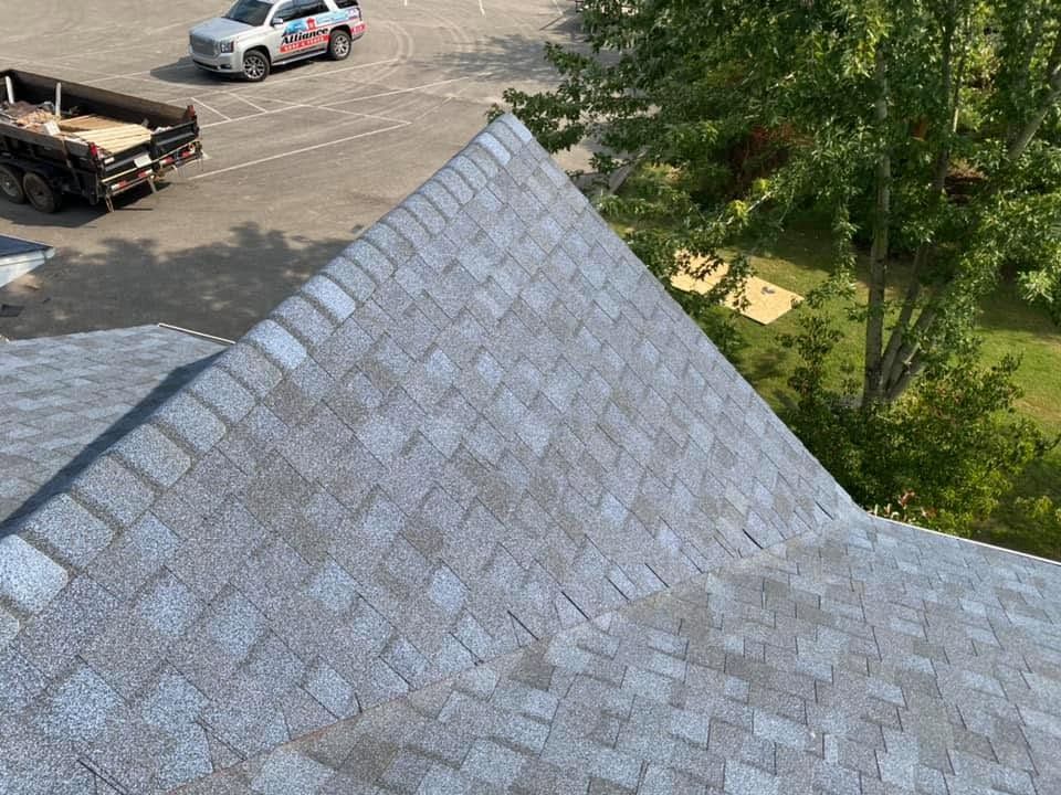 Steep gray shingled roof beside a parking lot with vehicles and trees
