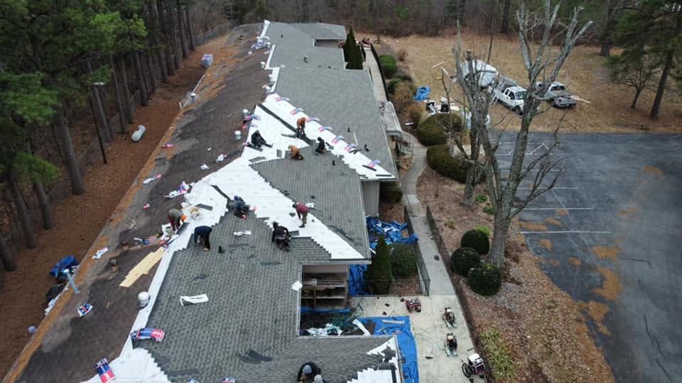 Aerial view of a roof with workers repairing shingles and scattered materials near a driveway and trees