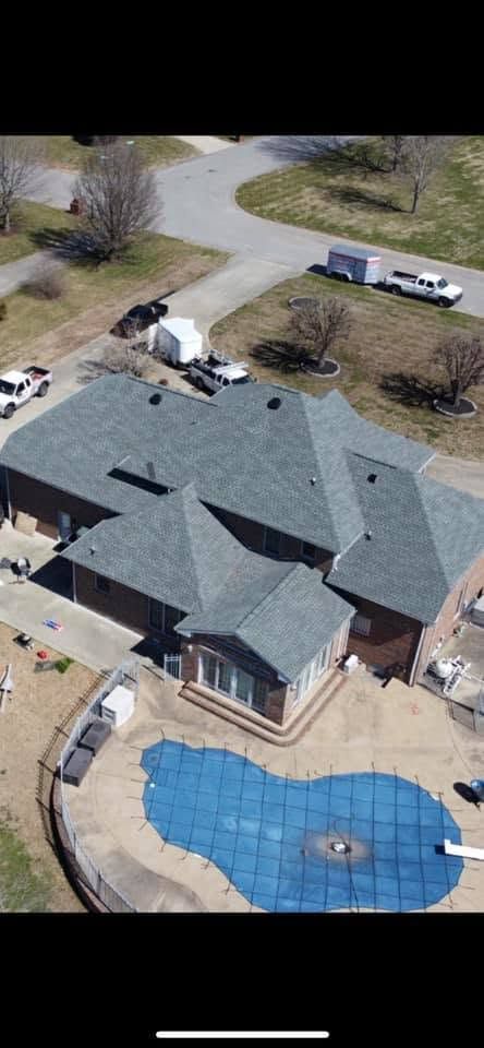 Aerial view of a house with a dark roof, driveway, and a blue backyard pool.
