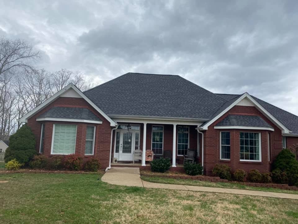 Brick ranch house with dark shingled roof, white-trimmed windows, and a front porch under cloudy skies