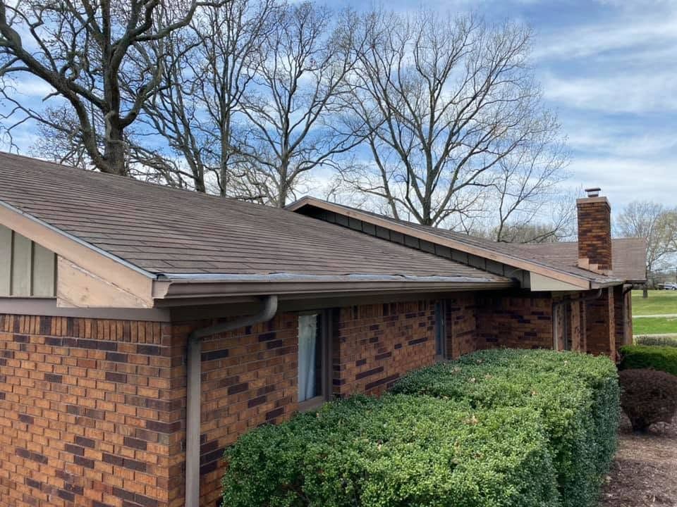 Brick townhouse exterior with brown roof, trimmed hedges, and leafless trees under a blue sky