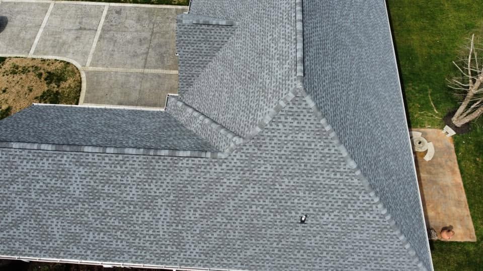 Aerial view of a gray shingled roof with a driveway and lawn beside it.