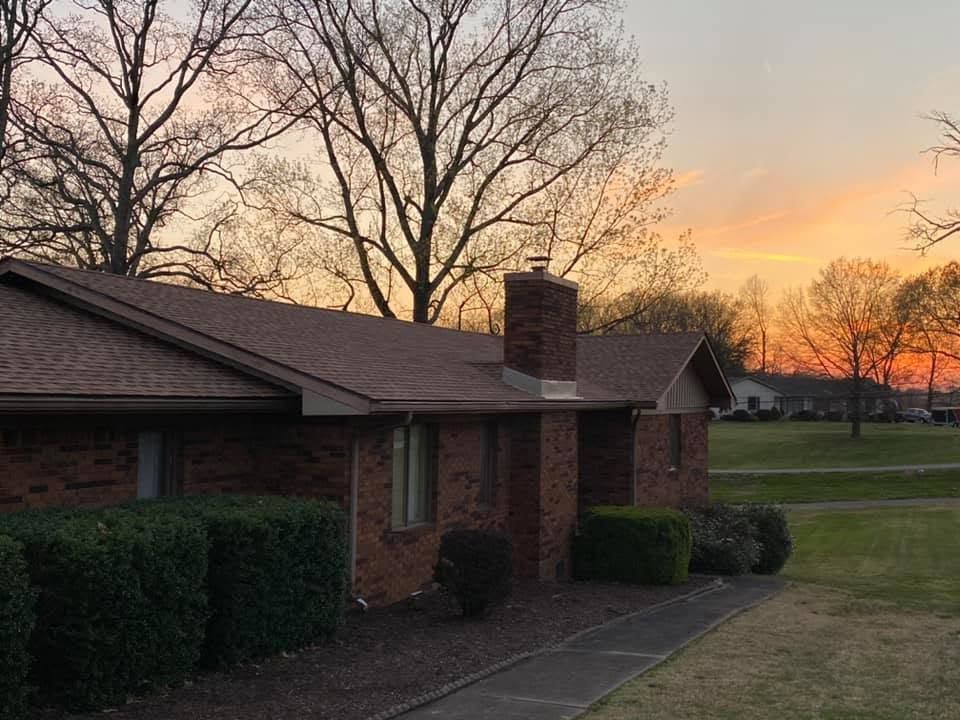 Brick house at sunset with leafless trees and a grassy yard