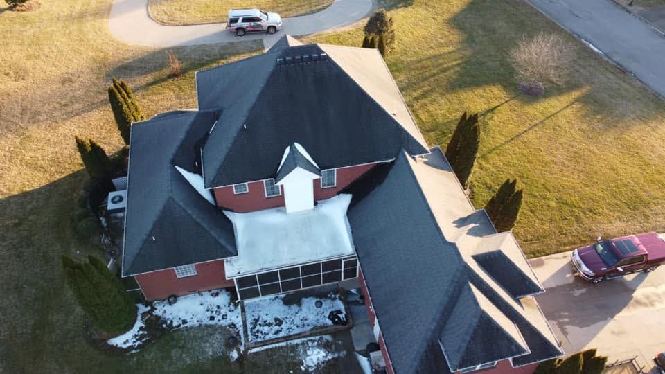Aerial view of a house with a dark roof, white siding, red garage, and cars parked nearby.
