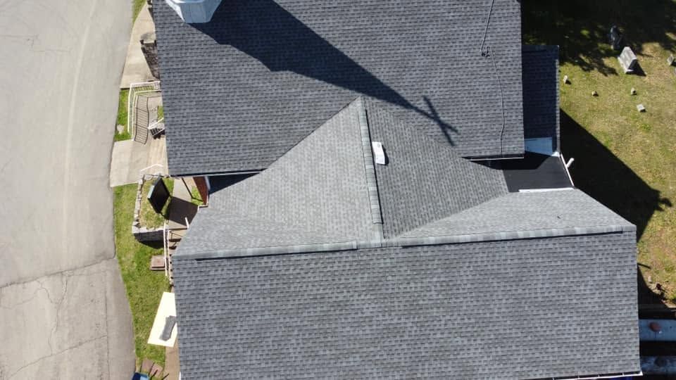 Aerial view of gray-roofed house and driveway beside a curved street and lawn