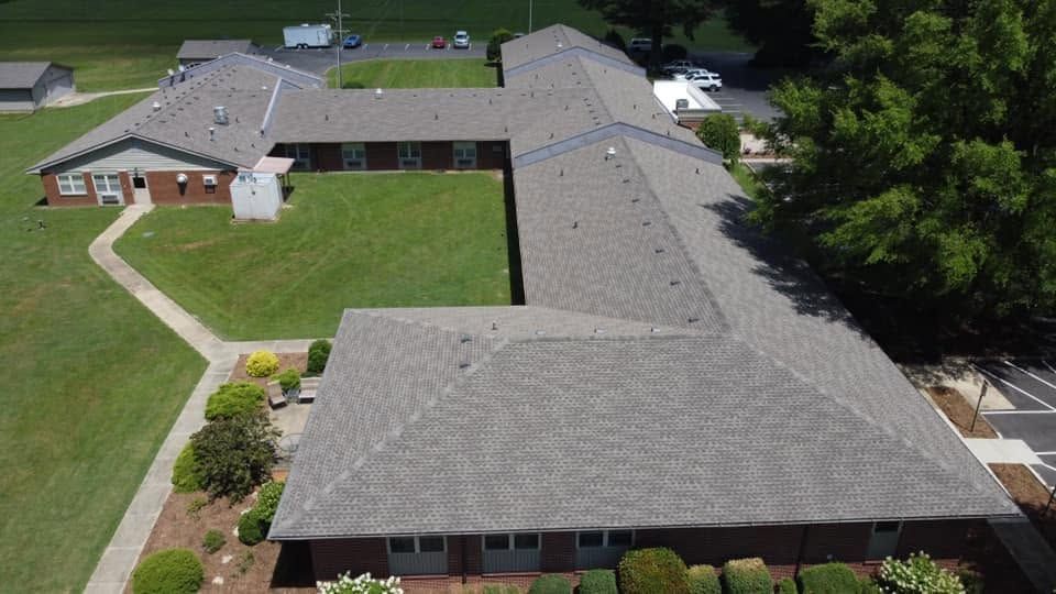 Aerial view of a large gray-roofed building with a grassy courtyard and surrounding trees.