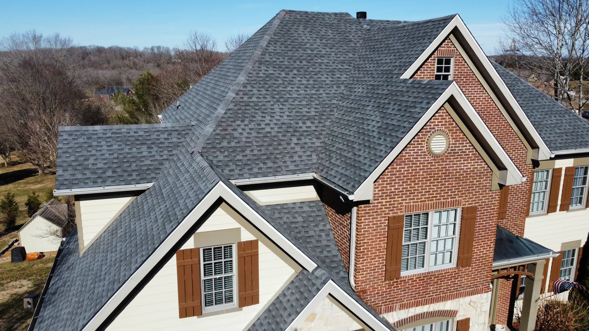 Brick house with dark gray shingled roof and white-trimmed windows viewed from above