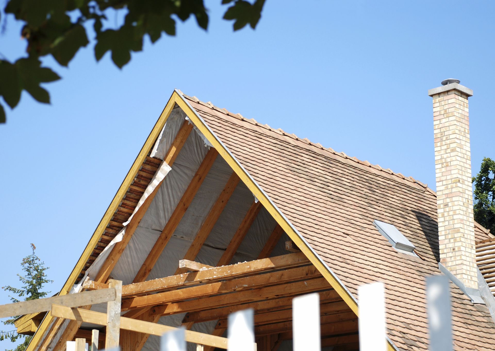 Partially built brick house with a steep tiled roof and chimney against a blue sky