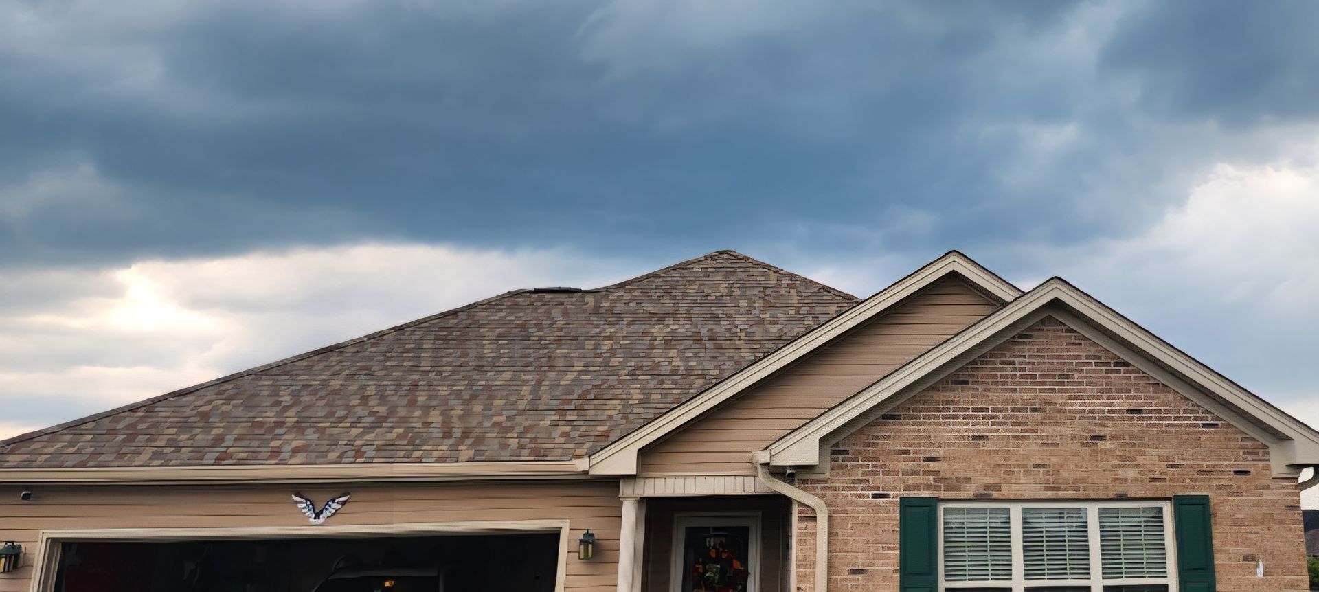 Suburban brick house with a shingled roof under cloudy skies