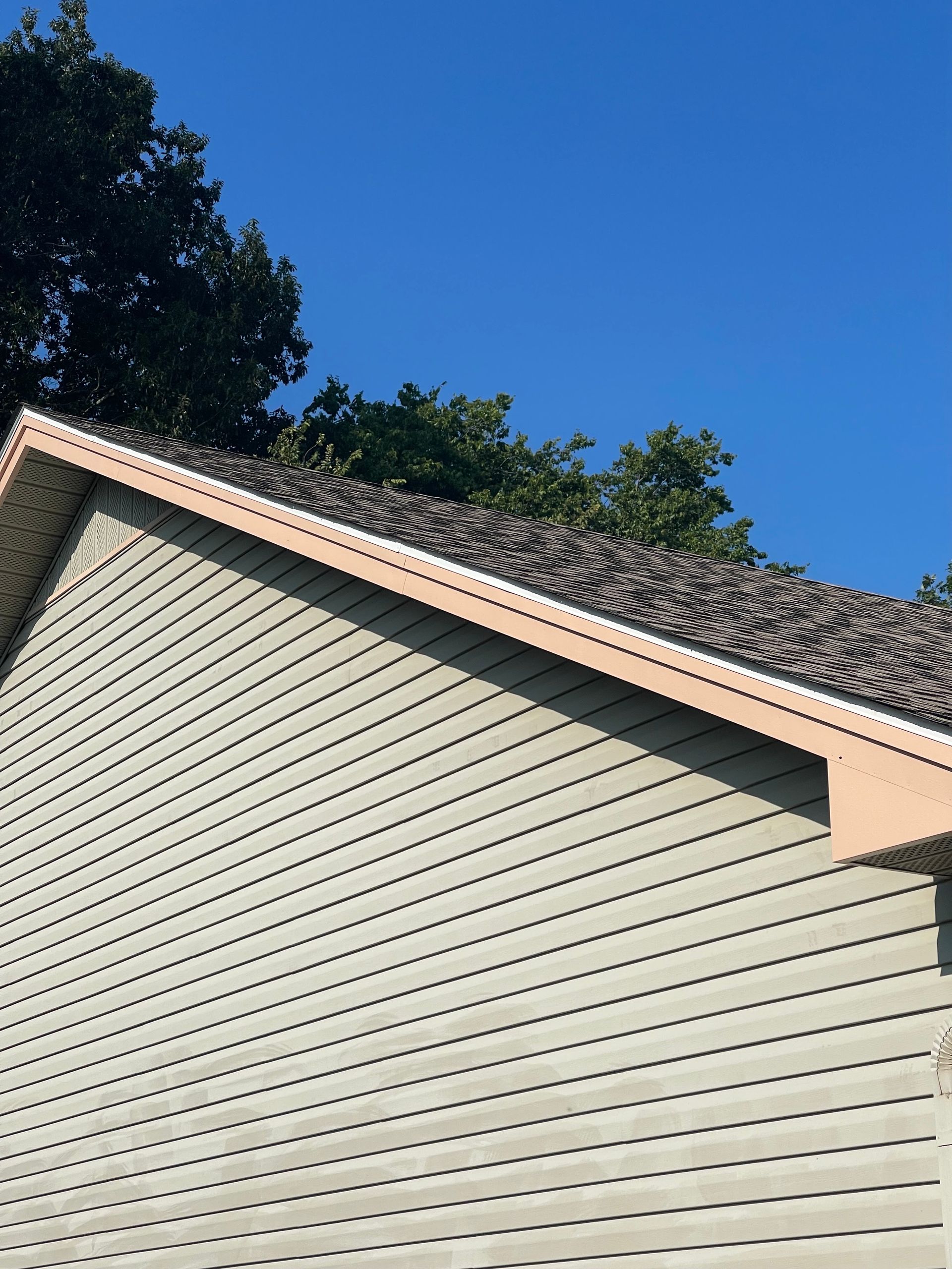 Side of a beige house with a shingled roof against a clear blue sky