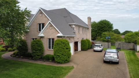 Suburban brick house with a curved driveway, two parked cars, and a green lawn
