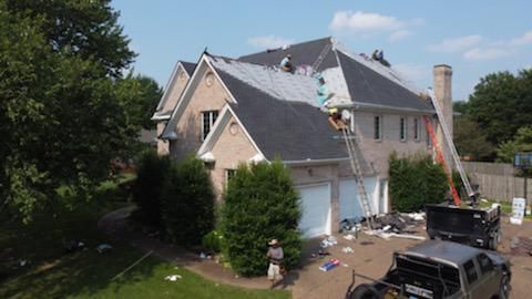 Suburban house with a gray roof, white garage, and construction debris in the driveway under sunny skies