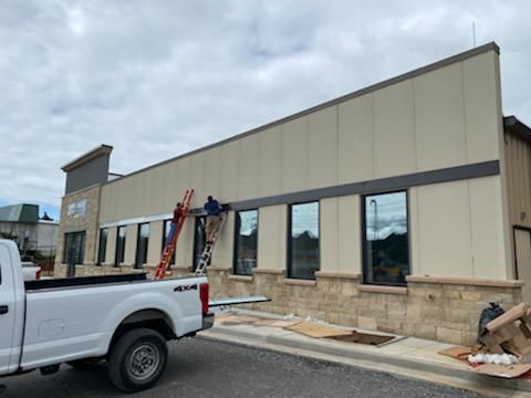 Construction workers on a beige commercial building exterior beside a white pickup truck.