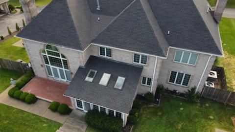 Aerial view of a large gray suburban house with a dark roof, white trim, and a front porch.