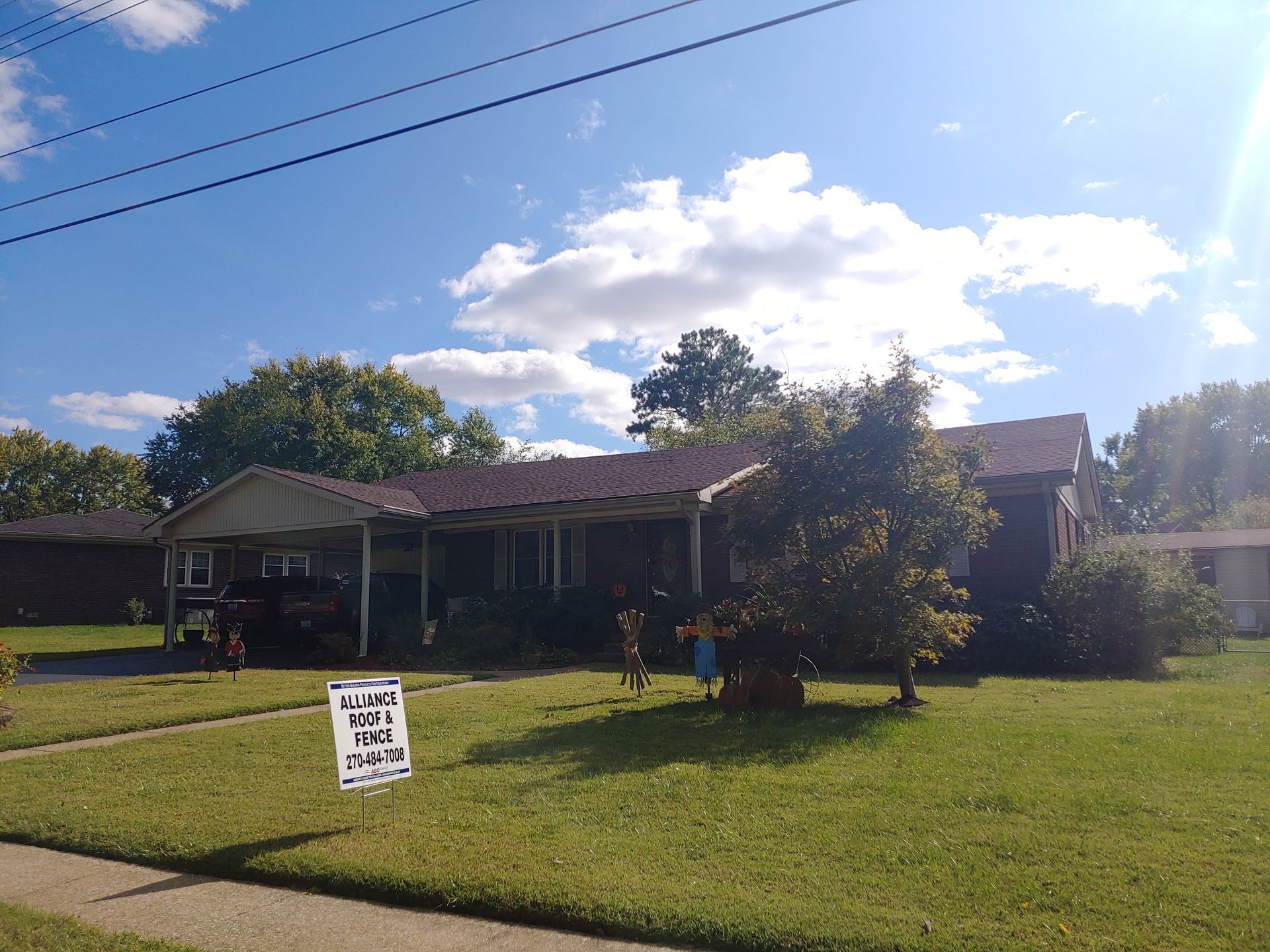 Front lawn of a single-story house with a white yard sign under a bright blue sky