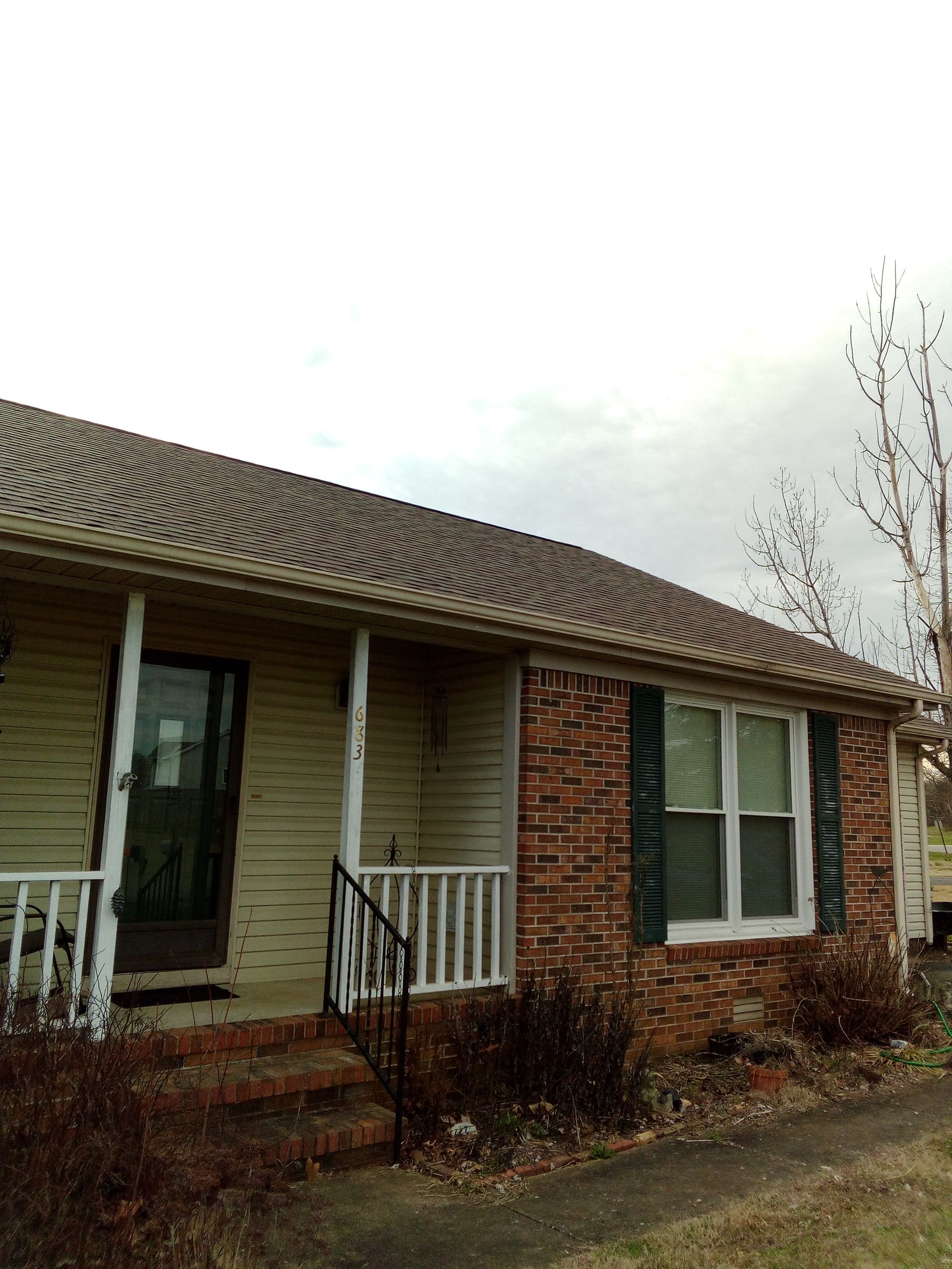 Single-story brick house with a small front porch, white railing, and bare tree outside.