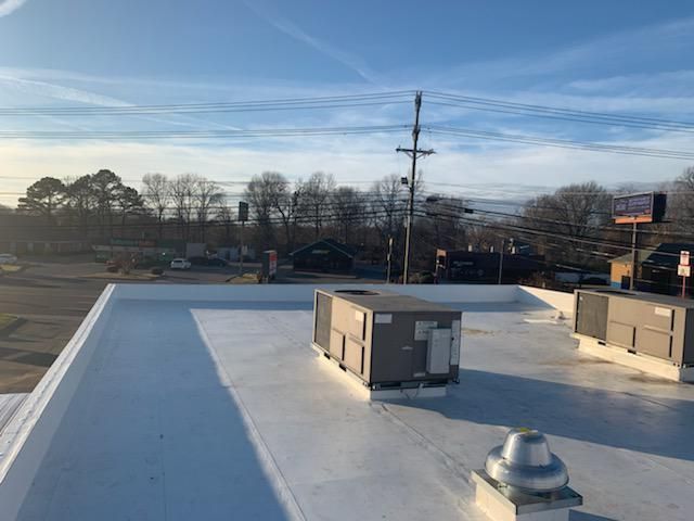 Flat white rooftop with HVAC units under a blue sky, viewed from above.