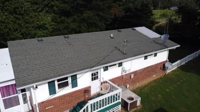 Aerial view of a single-story brick house with a gray roof and white trim, beside a fenced green yard.