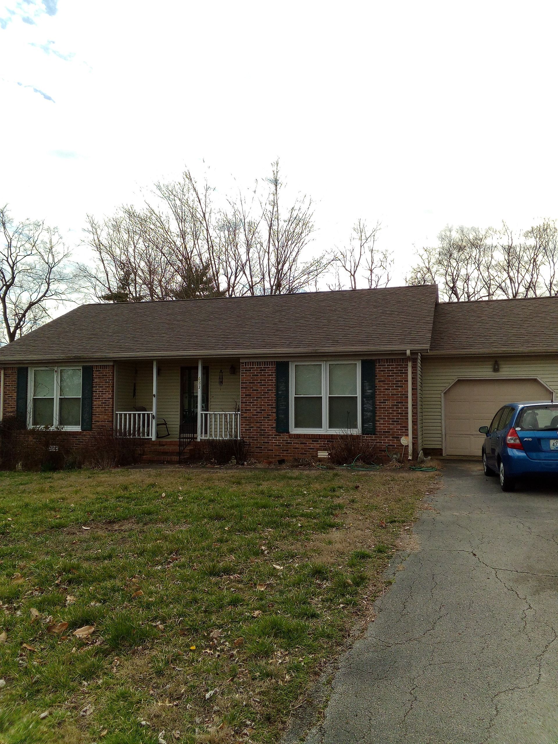 Single-story brick house with a car in the driveway and a front lawn.