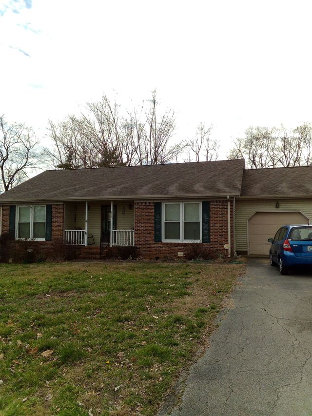 Single-story brick house with a front lawn, driveway, and blue car parked beside the garage.