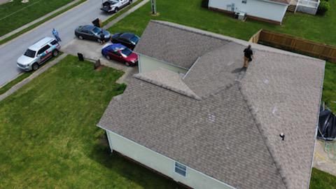 Aerial view of a suburban house with cars parked along the street and a person on the roof.