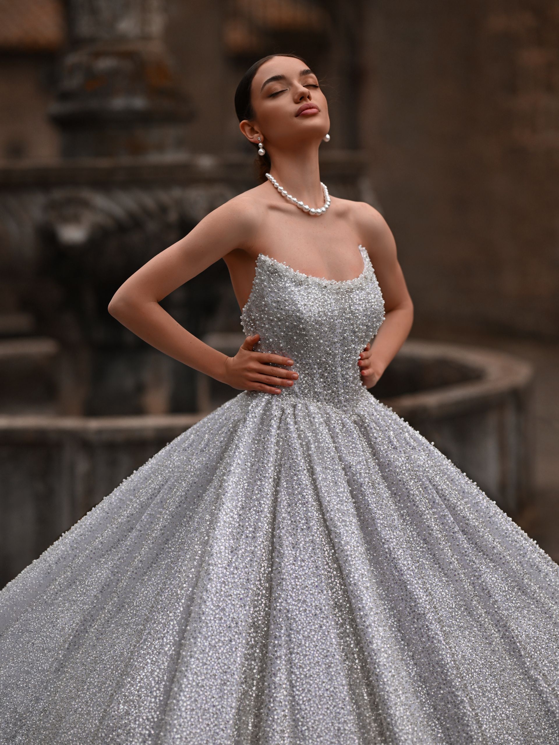 Woman in a sparkling silver ball gown posing in front of a fountain outdoors