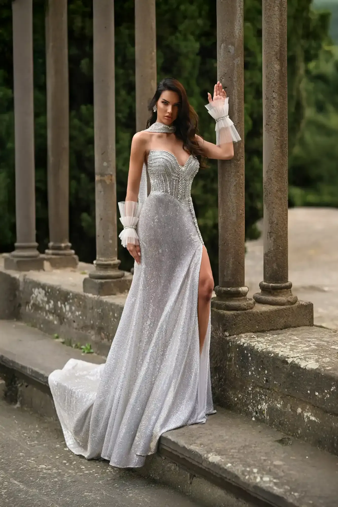 Woman in a silver gown and white gloves posing on stone steps by columns