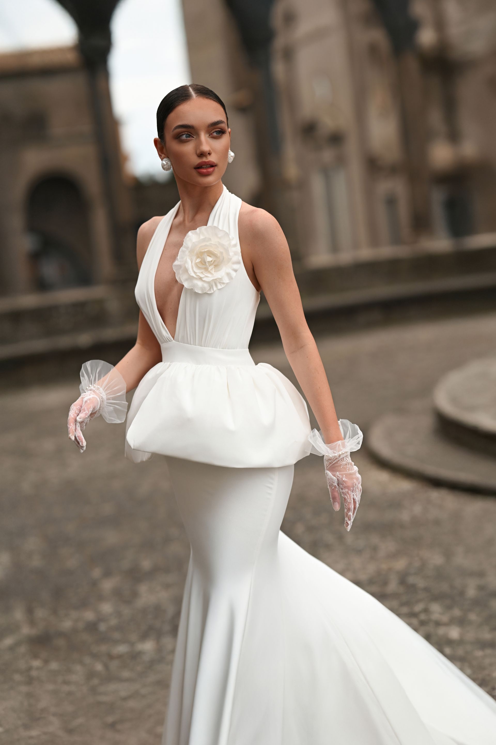 Woman in a white bridal gown posing on a stone street before a historic building.