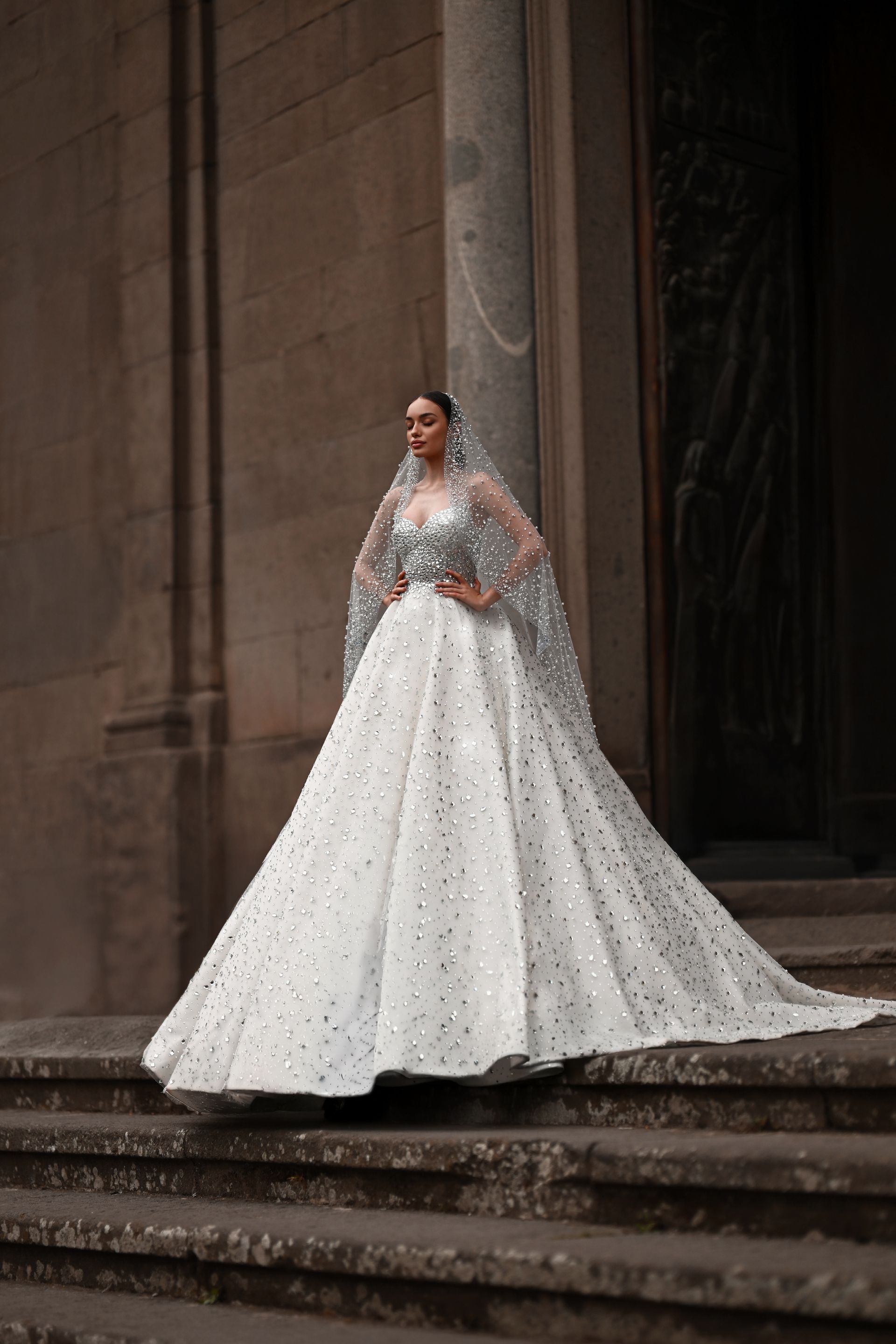 Bride in a white embroidered gown standing on stone steps outside a grand building