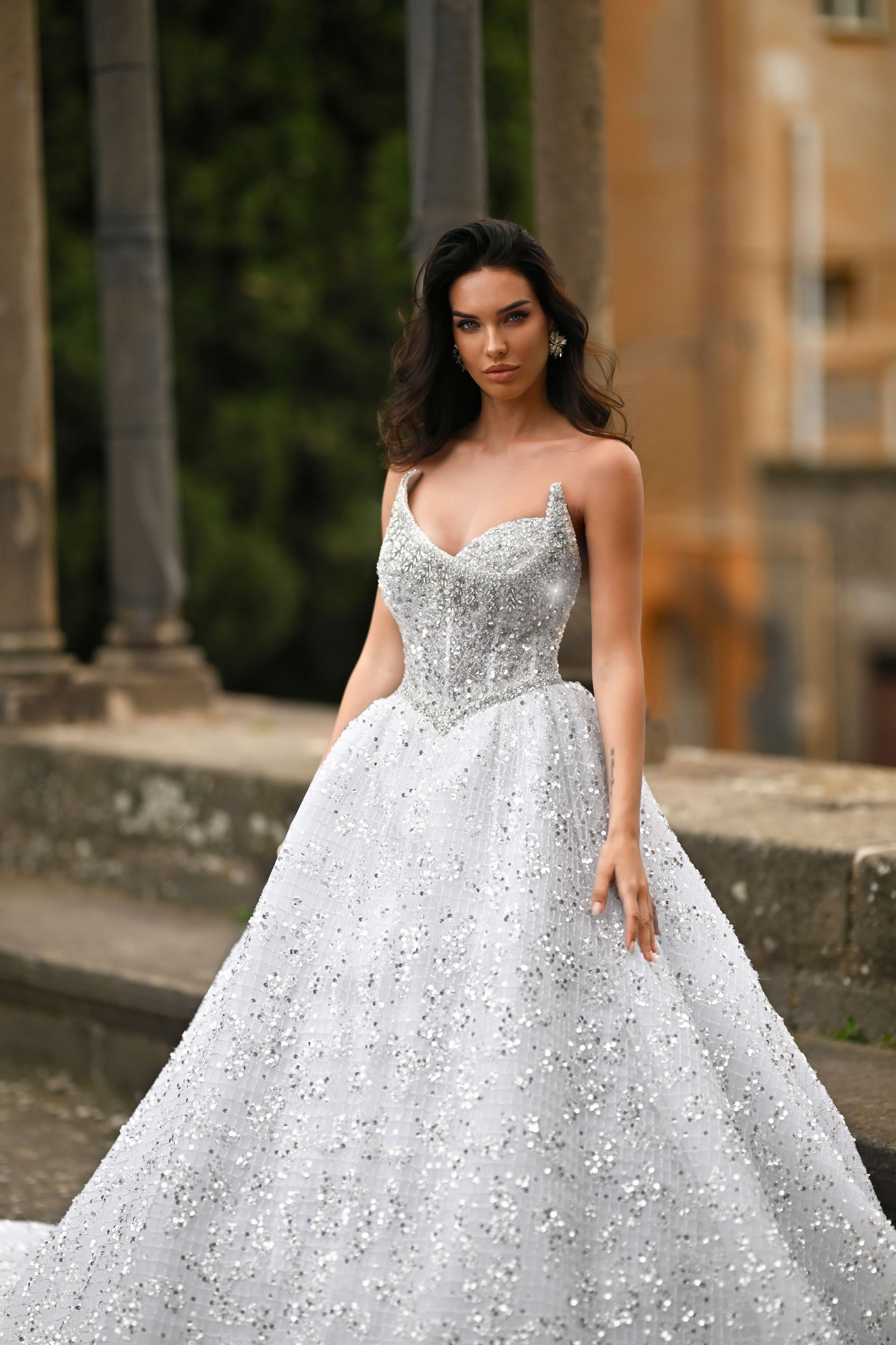 Woman in a sparkling white ball gown standing outdoors on a stone walkway
