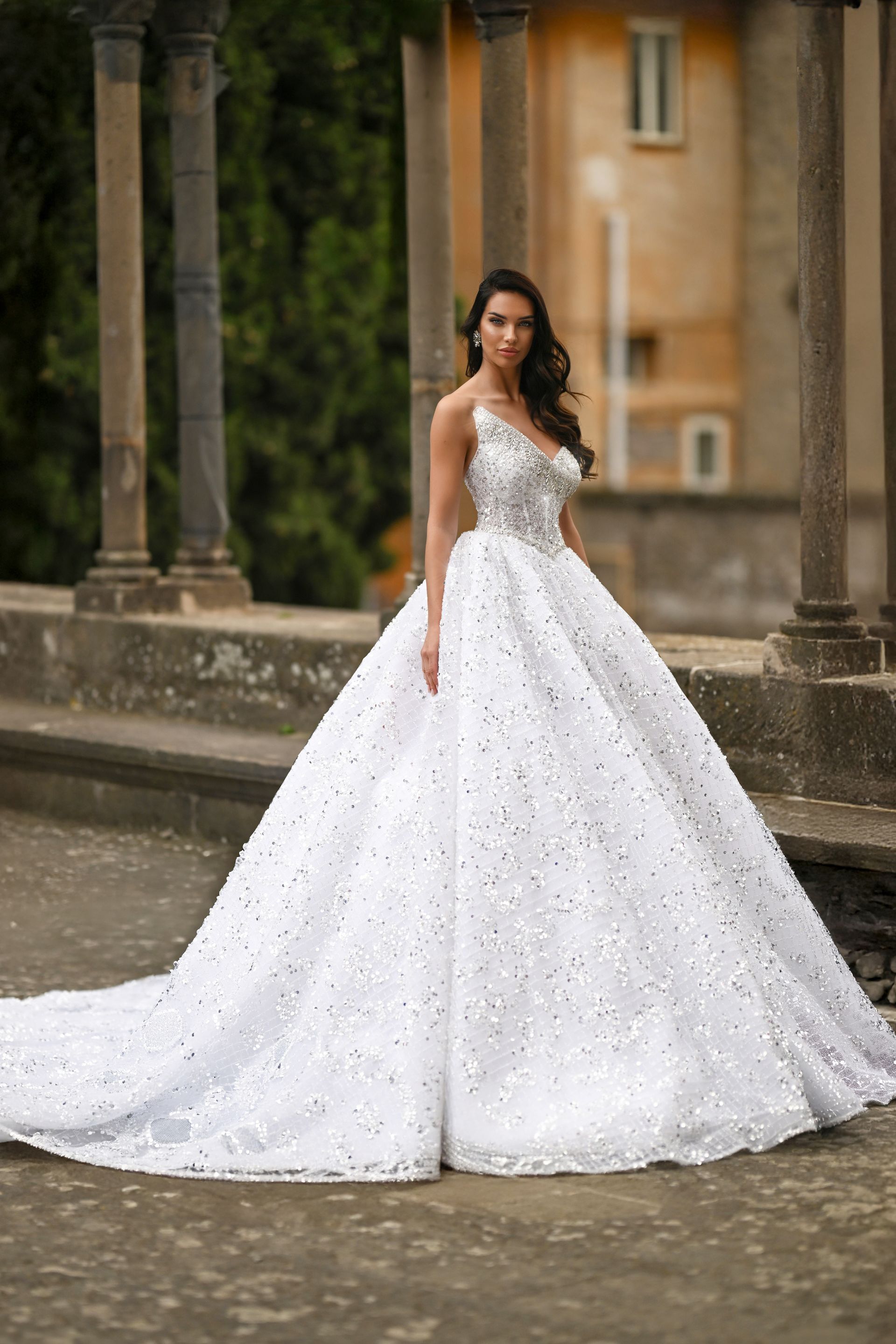 Bride in a white ball gown standing in a courtyard with stone columns and arches