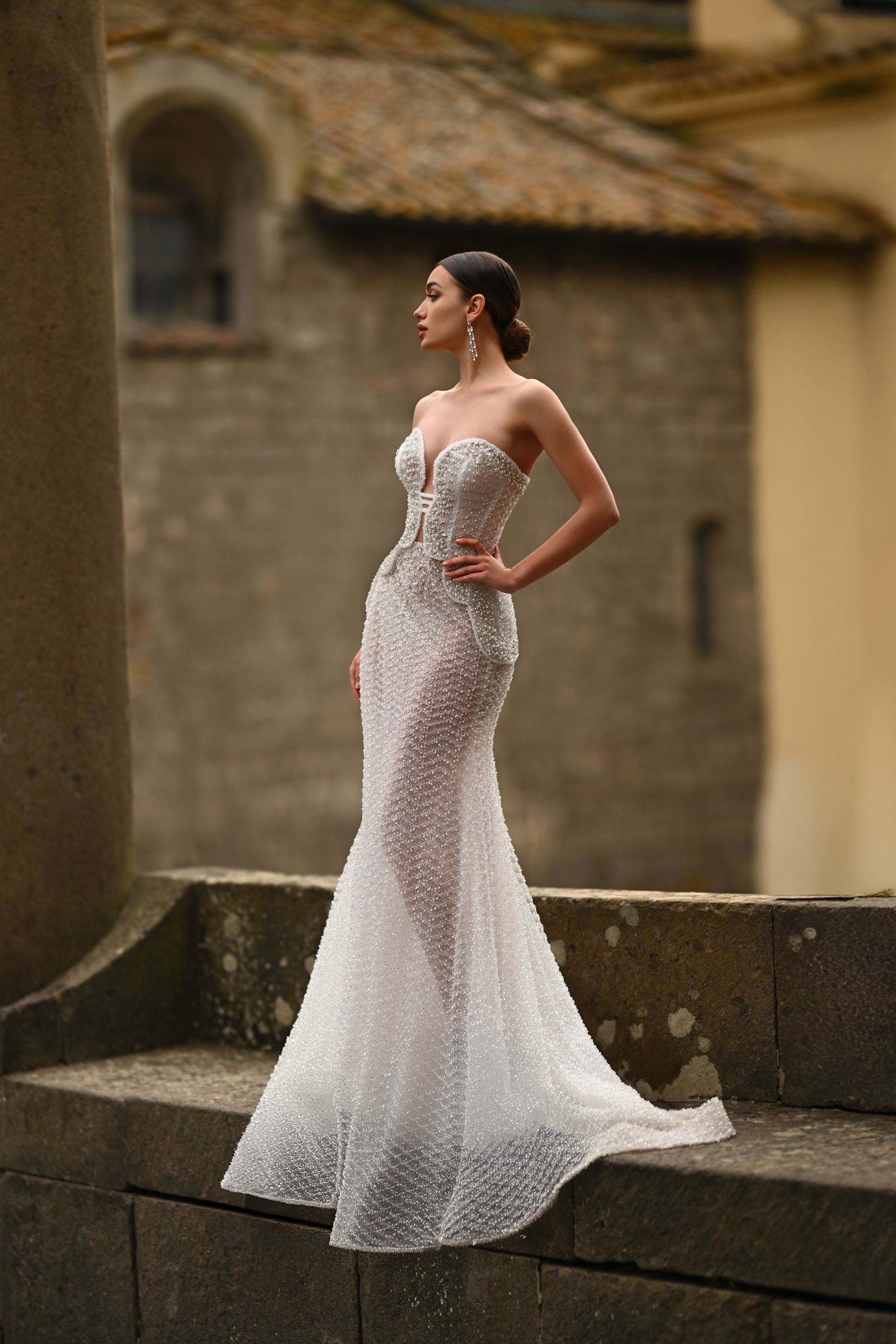 Woman in a shimmering strapless gown posing on stone steps outdoors