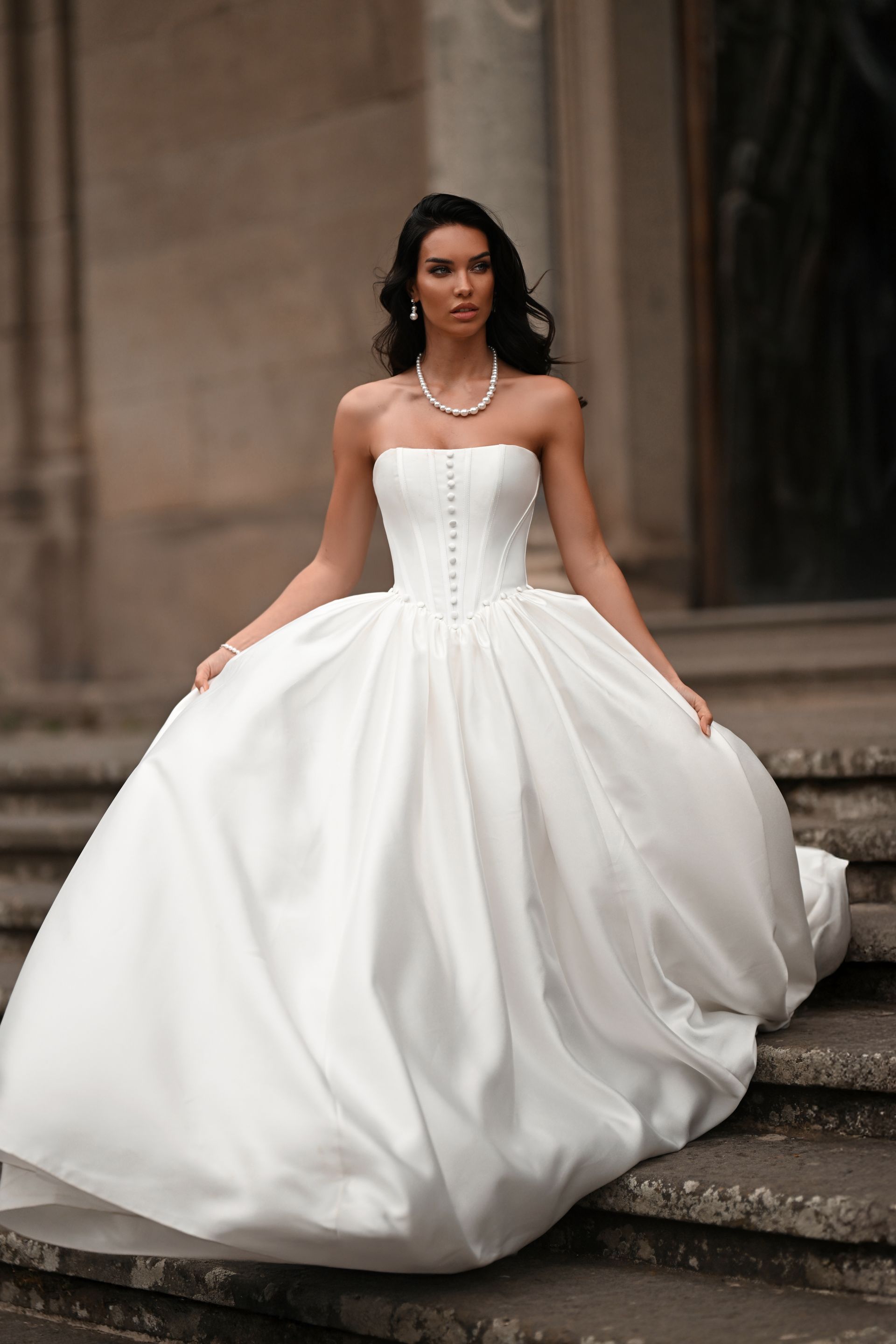 Woman in a strapless white ball gown standing on stone steps outdoors